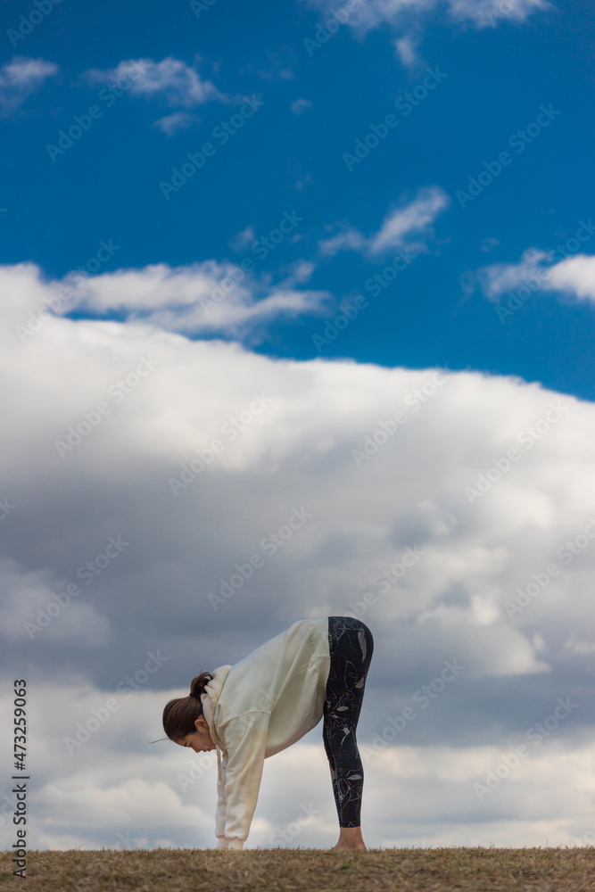 秋の公園でヨガを練習している若い女性ヨガインストラクターの姿と綺麗な青空の風景
