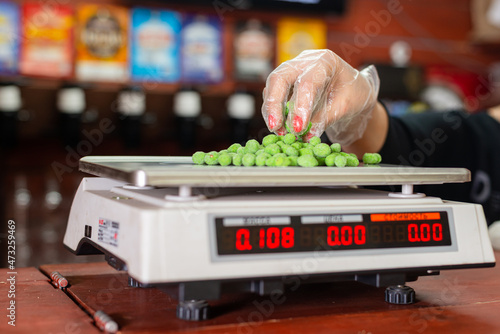 On an electronic scale, the seller weighs salted nuts, in the background is a beer showcase