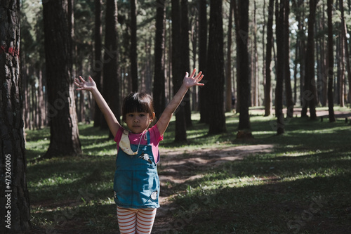 Active little girls running in the pine forest on a warm summer day. Happy girl smiles and laughs while spending time with her family in the park on vacation.
