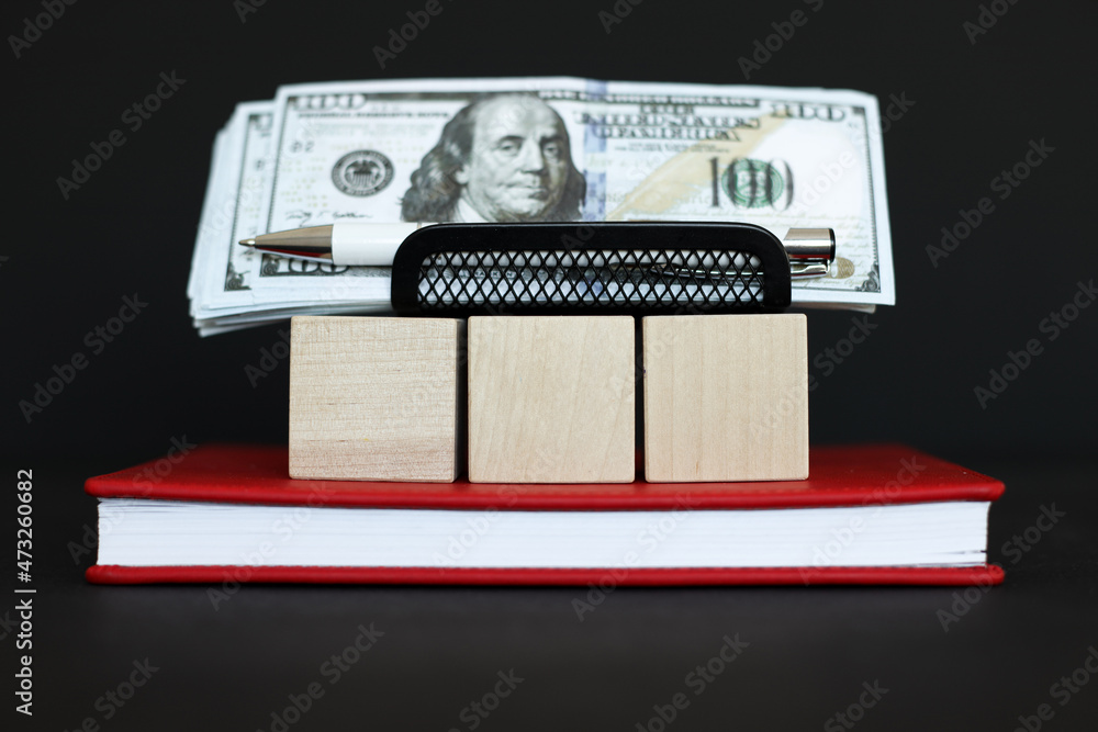 Three wooden cubes stacked on top of each other with copy space on the right. On a black background. red notebook. money Three wooden cubes stacked on top of each other with copy space on the right. On a black background. red notebook. money