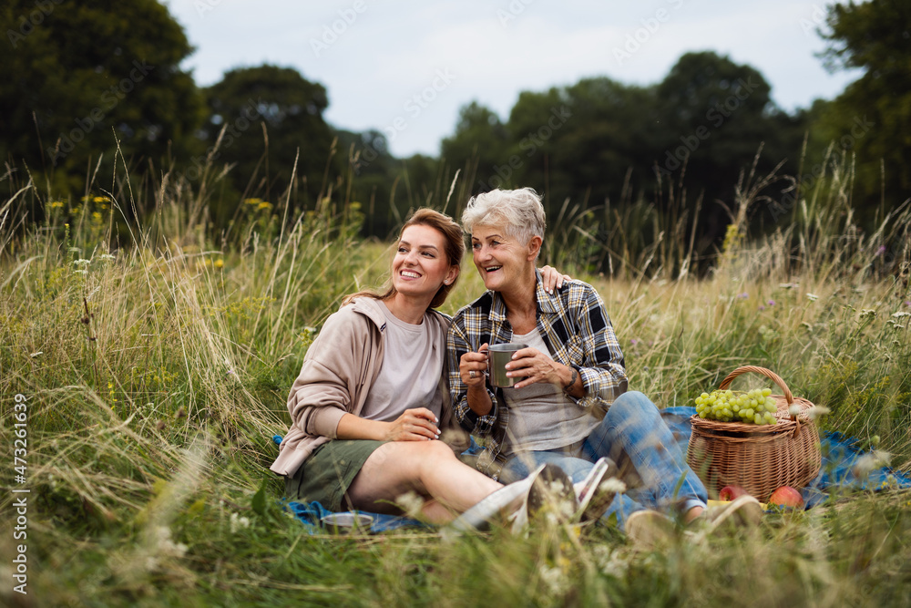 Happy senior mother and adult daughter sitting and having picnic outdoors in nature, talking. Happy senior mother and adult daughter sitting and having picnic outdoors in nature, talking.