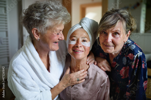 Happy senior women friends in bathrobes looking at camera indoors at home, selfcare concept.