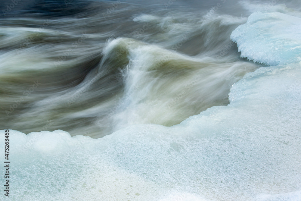 Long exposure shot of fast flowing wintry river with ice banks - obrazy, fototapety, plakaty 