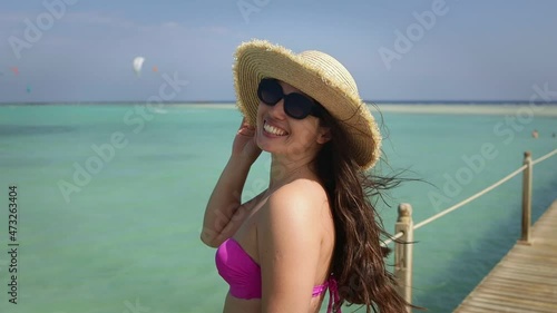 smiling young woman in sunglasses and straw hat with hair blowing in the wind