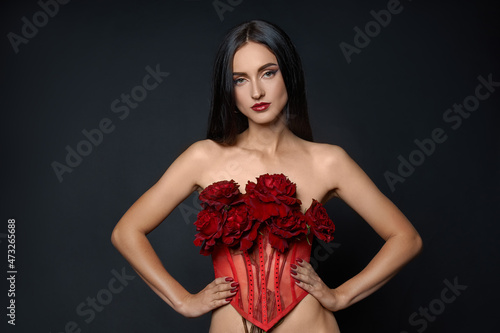 Beautiful brunette woman with a bouquet of red rose flowers in red corset. Long hair, nude slim body art portrait