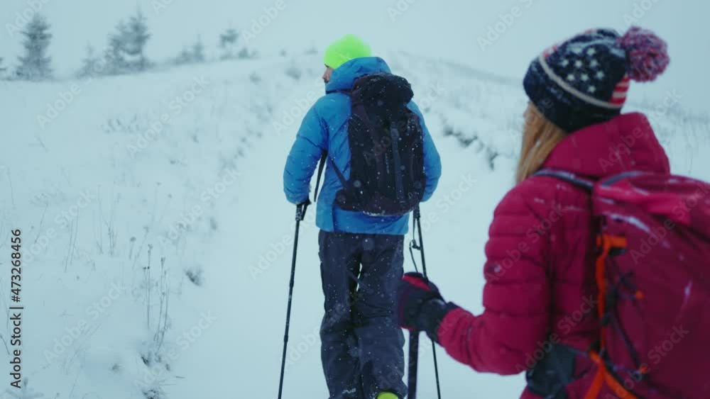 Lviv, Ukraine - January 19, 2021: Close up shot back woman and man walk in the winter mountains in forest road with trekking poles. Sport healthy cold weather hiker climbing. Slow motion Lviv, Ukraine - January 19, 2021: Close up shot back woman and man walk in the winter mountains in forest road with trekking poles. Sport healthy cold weather hiker climbing. Slow motion