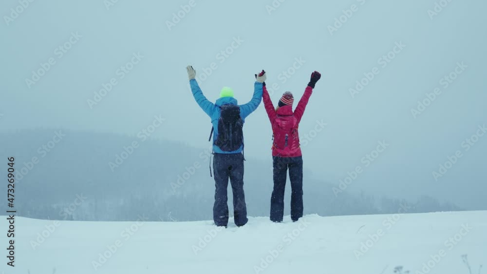 Lviv, Ukraine - January 19, 2021: Happy couple with backpacks in snow mountains feel freedom on top. Raise your hands to the mountain. Rocks outdoor success cold exercise winter. Slow motion