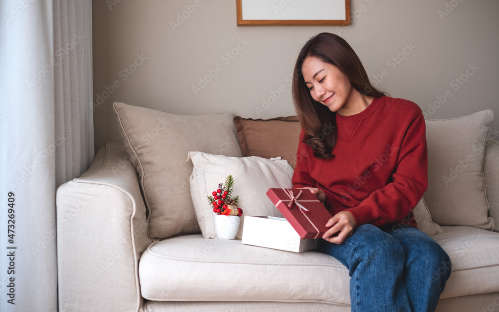 Portrait image of a young woman receiving and opening a red present box at home