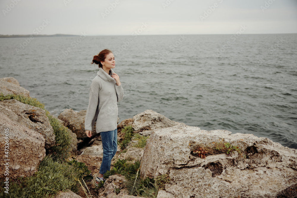 woman in a gray sweater stands on a rocky shore nature unaltered