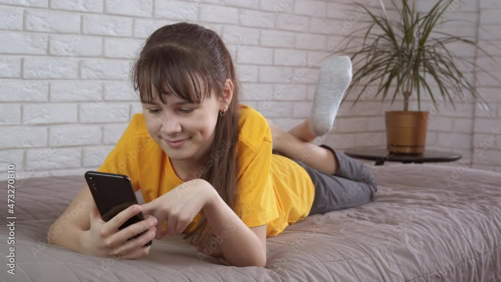 Teenager with a smartphone. Happy teenage girl lies on the couch with a smartphone in her hands. Teenagers smartphone addiction concept. Teenager with a smartphone. Happy teenage girl lies on the couch with a smartphone in her hands. Teenagers smartphone addiction concept.