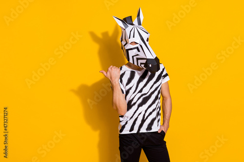 Photo of eccentric funky man wear zebra print t-shirt mask pointing thumb finger empty space isolated yellow color background photo