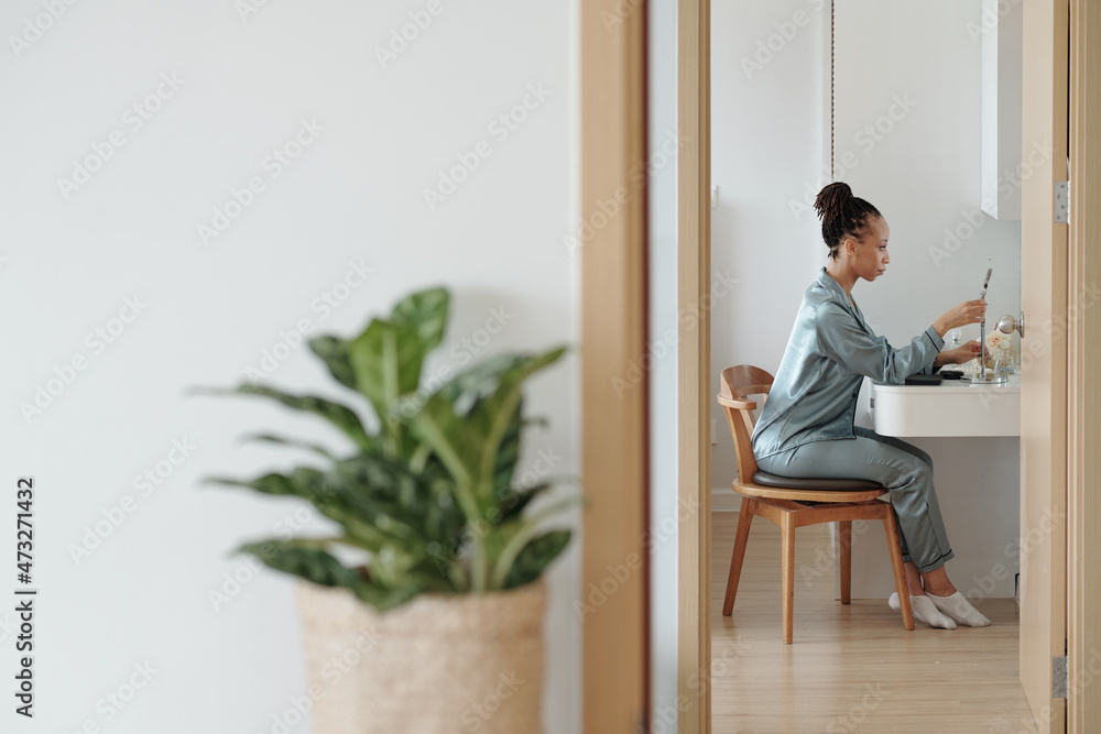 Fototapeta premium Beautiful woman in loungewear setting magnifying mirror at vanity in her bedroom