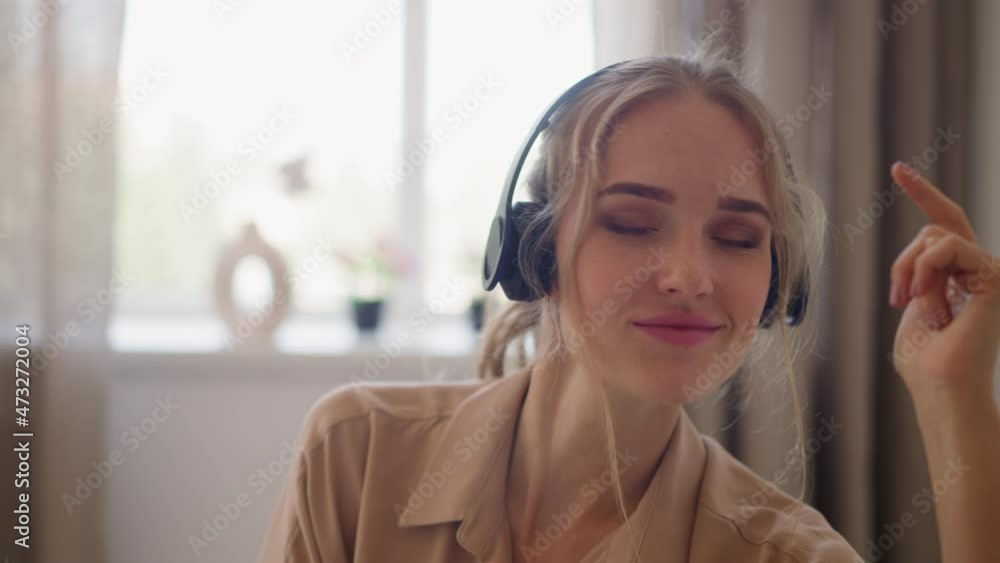 Young blonde haired woman with ponytail in headphones enjoys music moving to beat against bright window in comfortable home room slow motion closeup Young blonde haired woman with ponytail in headphones enjoys music moving to beat against bright window in comfortable home room slow motion closeup