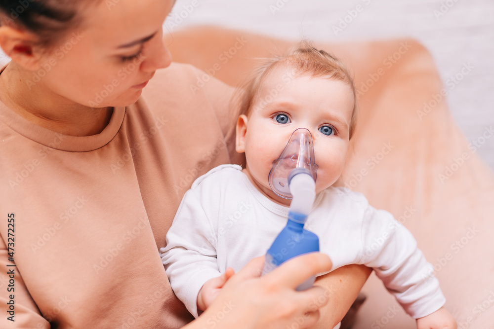 A little girl inhales from an inhaler with a nebulizer at home. A child with a viral disease in an inhalation mask is sitting in his mother's arms. Patient with asthma A little girl inhales from an inhaler with a nebulizer at home. A child with a viral disease in an inhalation mask is sitting in his mother's arms. Patient with asthma