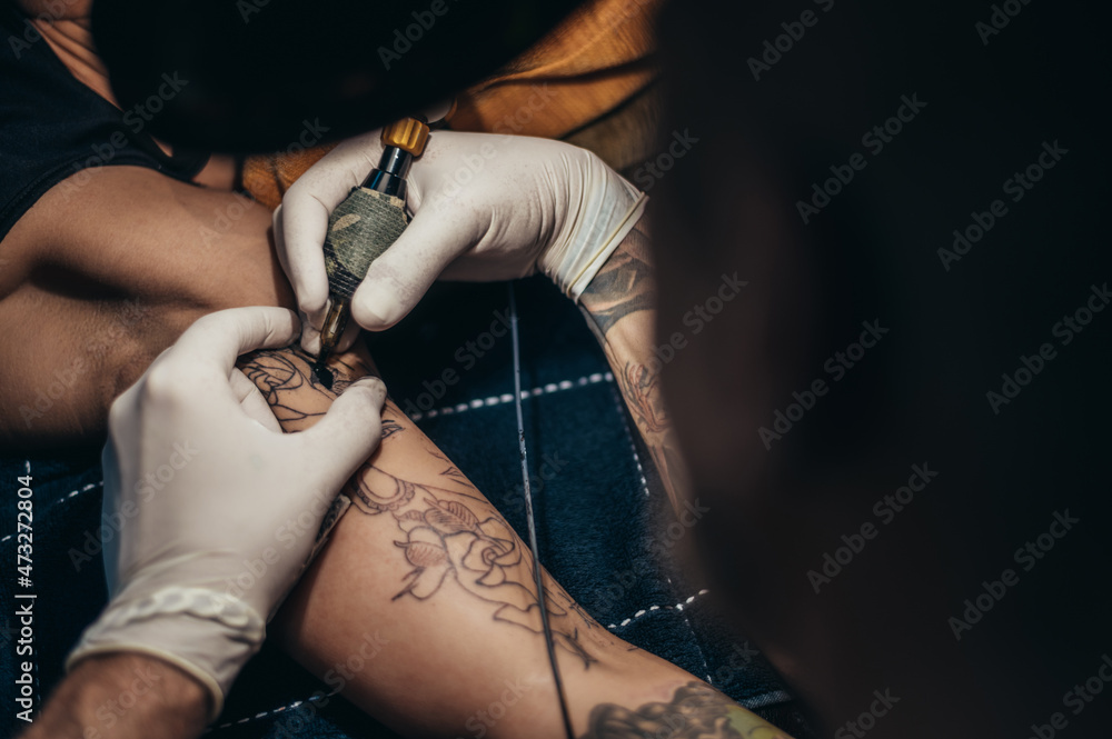 Tattoo artist hands in a white gloves holding a machine while creating a tattoo