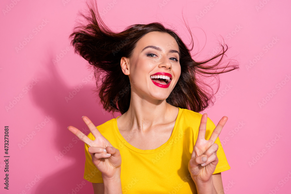 Photo of charming excited young woman wear yellow outfit air blowing showing two v-signs smiling isolated pink color background Photo of charming excited young woman wear yellow outfit air blowing showing two v-signs smiling isolated pink color background