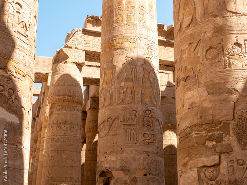 Tall columns with Egyptian hieroglyphs and symbols in the Karnak temple against the blue sky. Luxor, Egypt.