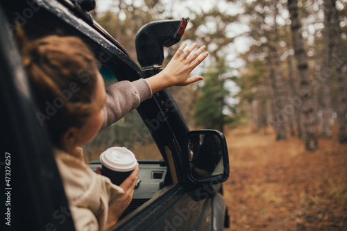 Millennial woman travelling off-road by car in a forest, drinking coffee, enjoying wind. Wanderlust concept. photo