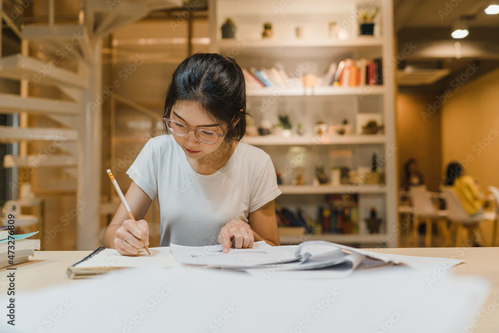 Asian student women reading books in library at university. Young undergraduate girl do homework, read textbook, study hard for knowledge on lecture desk at college campus overtime night. Asian student women reading books in library at university. Young undergraduate girl do homework, read textbook, study hard for knowledge on lecture desk at college campus overtime night.
