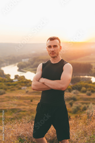A nice portrait of a young muscled man looking serious at the camera on a hill sunbathed .