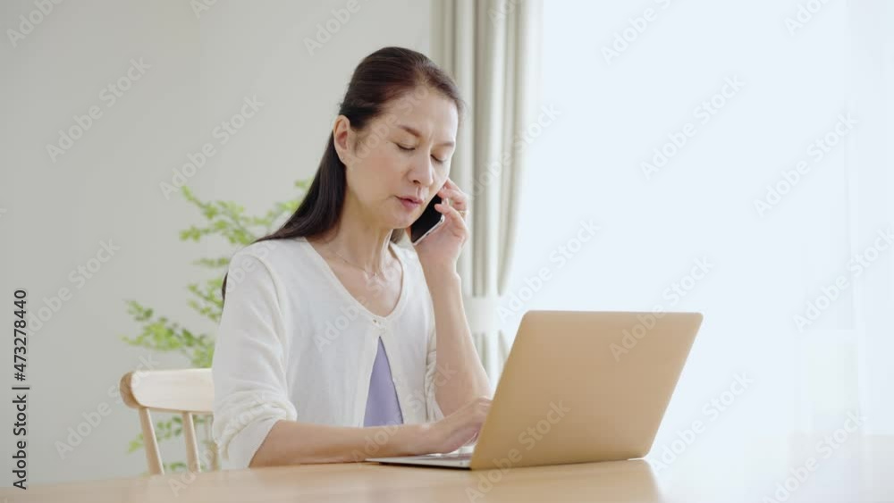 60p　パソコンを見ながらスマホで電話するシニア女性