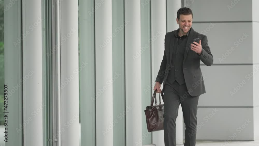 Happy businessman walking in front of the office building with a briefcase, looking at the mobile phone and getting a good news, jumping up excitedly Dance to celebrate Happy businessman walking in front of the office building with a briefcase, looking at the mobile phone and getting a good news, jumping up excitedly Dance to celebrate