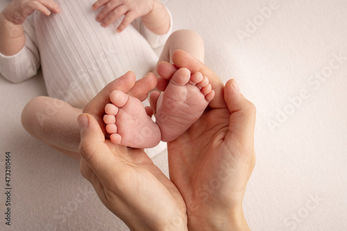 The palms of the father, the mother are holding the foot of the newborn baby. Feet of the newborn on the palms of the parents. Studio photography of a child's toes, heels and feet. 