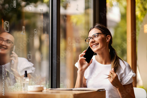 A happy college girl sitting in a coffee shop during her pause, taking and flirting on the phone. A college girl having a phone call in a coffee shop