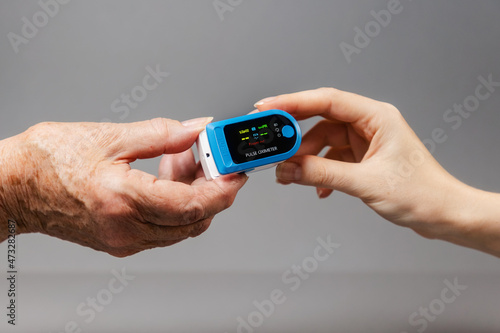 Φωτογραφία The hands of a young and an elderly woman hold an oximeter