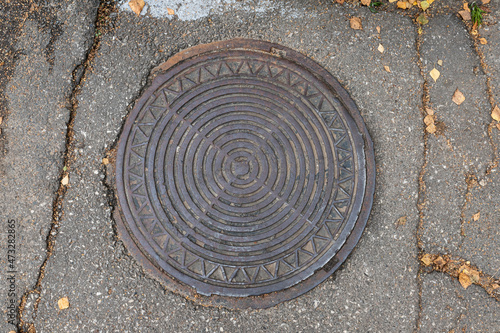 Old shabby round manhole cover on the city street