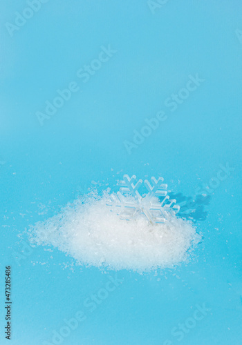 A crystal snowflake in a pile of snow on a blue background. Minimal winter concept..