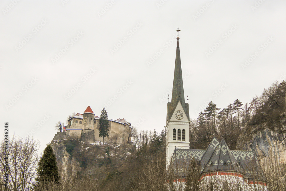 Bled campanile della chiesa di San Martino tra gli alberi e il castello con neve