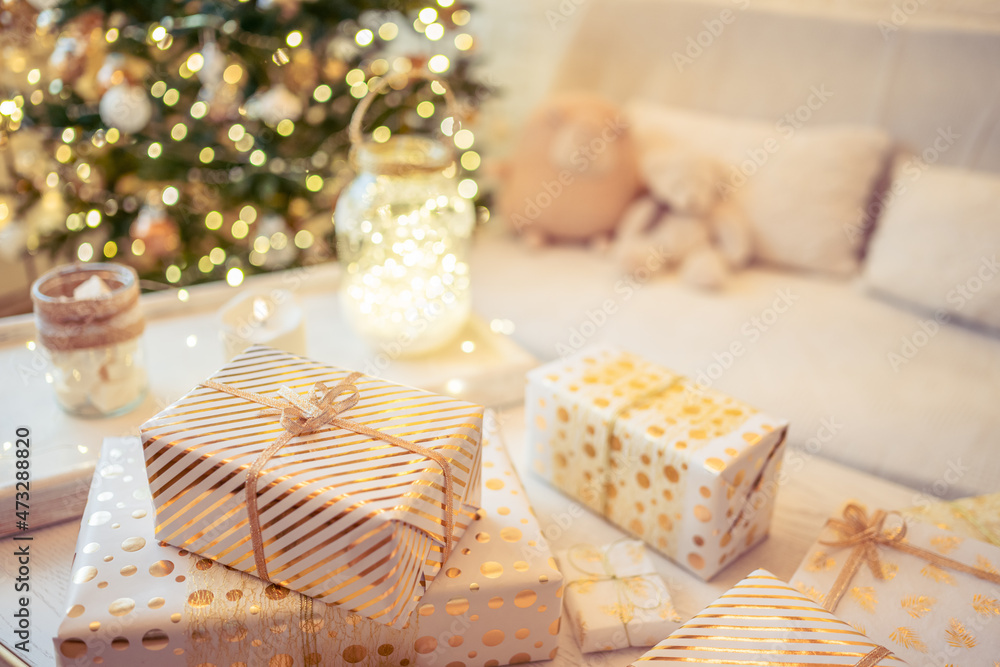A lot of packing handmade gift boxes lying on the table near Christmas tree in the midst of golden lights, glowing garland, candle. Soft focus A lot of packing handmade gift boxes lying on the table near Christmas tree in the midst of golden lights, glowing garland, candle. Soft focus