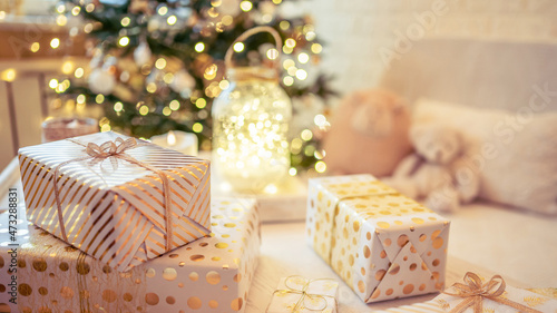 A lot of packing handmade gift boxes lying on the table near Christmas tree in the midst of golden lights, glowing garland, candle. Soft focus. 16:9