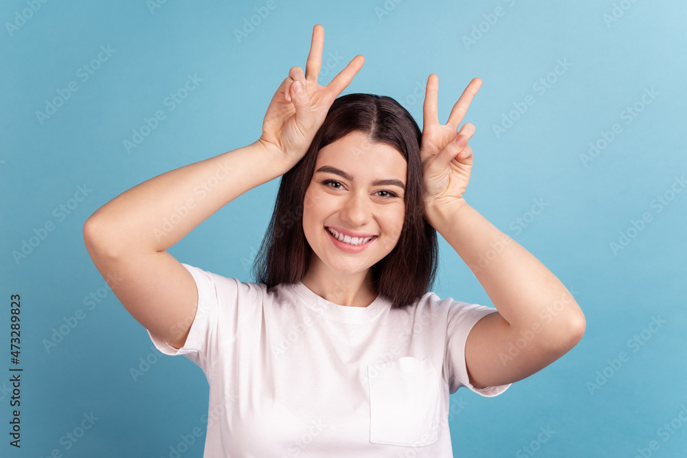 Photo of young pretty girl have fun show fingers pet ears playful grimacing isolated over blue color background
