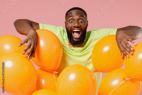 Young overjoyed cool crazy black gay man 20s in green t-shirt bow tie hold bunch of air inflated helium balloons celebrating birthday party isolated on plain pastel pink background studio portrait © ViDi Studio