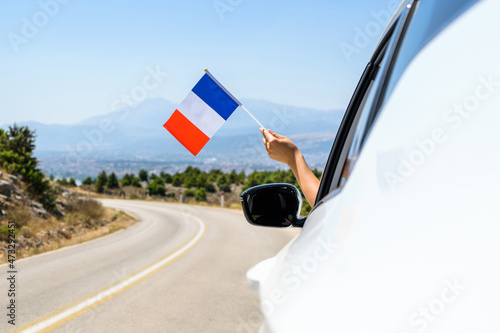 Woman holding France flag from the open car window driving along the serpentine road in the mountains. Concept