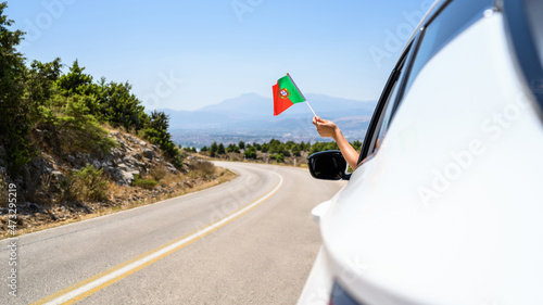 Woman holding Portugal flag from the open car window driving along the serpentine road in the mountains. Concept