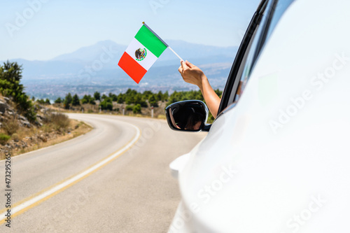 Woman holding Mexico flag from the open car window driving along the serpentine road in the mountains. Concept