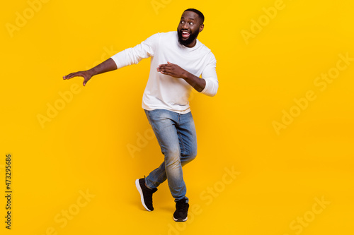 Full size photo of cheerful satisfied young man enjoy clubbing look empty space beaming smile isolated on yellow color background