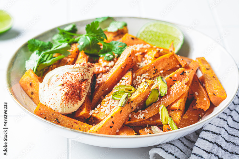 Baked sweet potato wedges with hummus, nuts and seeds in bowl. Healthy vegan food concept. Baked sweet potato wedges with hummus, nuts and seeds in bowl. Healthy vegan food concept.