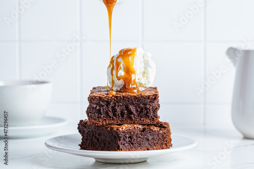 Fotografija Stack of brownie squares with scoop of ice cream and caramel, white background