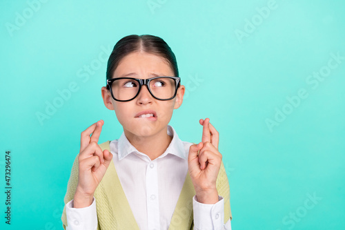 Photo of nervous little lady crossed fingers bite lip look empty space wear green top isolated teal color background