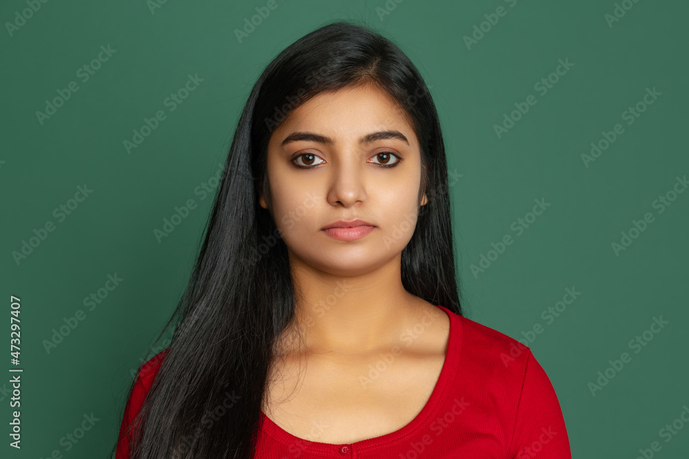 Fototapeta premium Close-up young beautiful serious girl, student looking at camera isolated on dark green studio backgroud