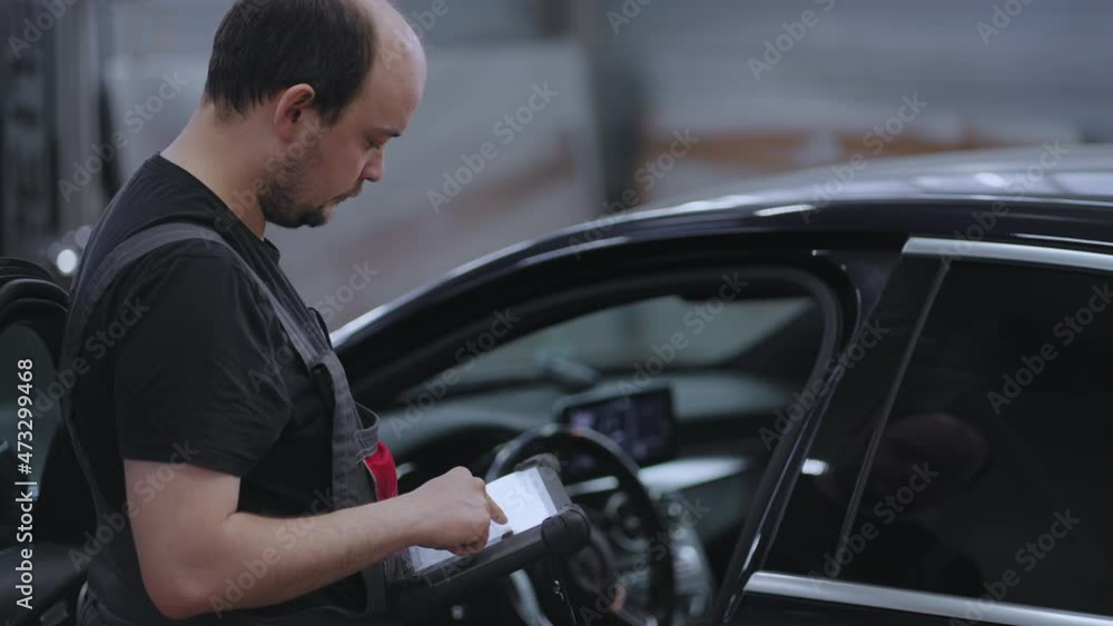 Portrait A mechanic in a car service close-up holds a tablet in his hands and presses on the screen near the car Portrait A mechanic in a car service close-up holds a tablet in his hands and presses on the screen near the car