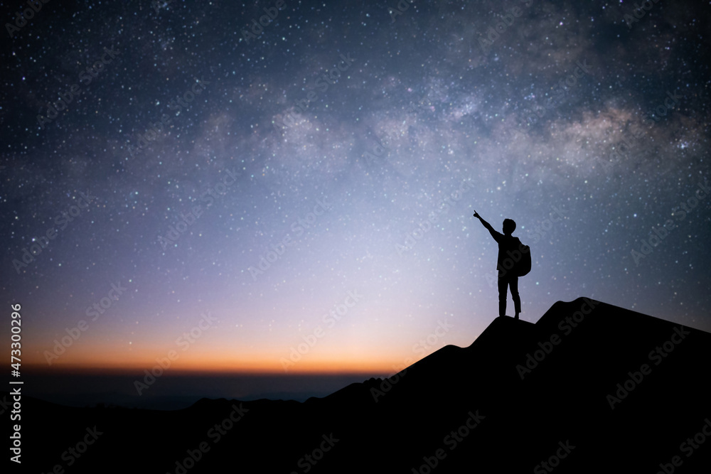 Silhouette of young traveler and backpacker raise your hand and point your finger at the stars and milky way in the sky. He enjoyed traveling and was successful when he reached the summit.