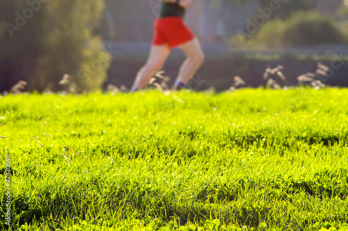 unfocused athlete man exercising in park with focused green grass in foreground