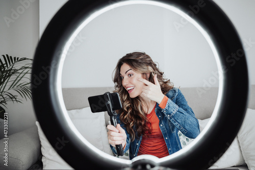 Smiling influencer with smart phone applying make-up at home studio