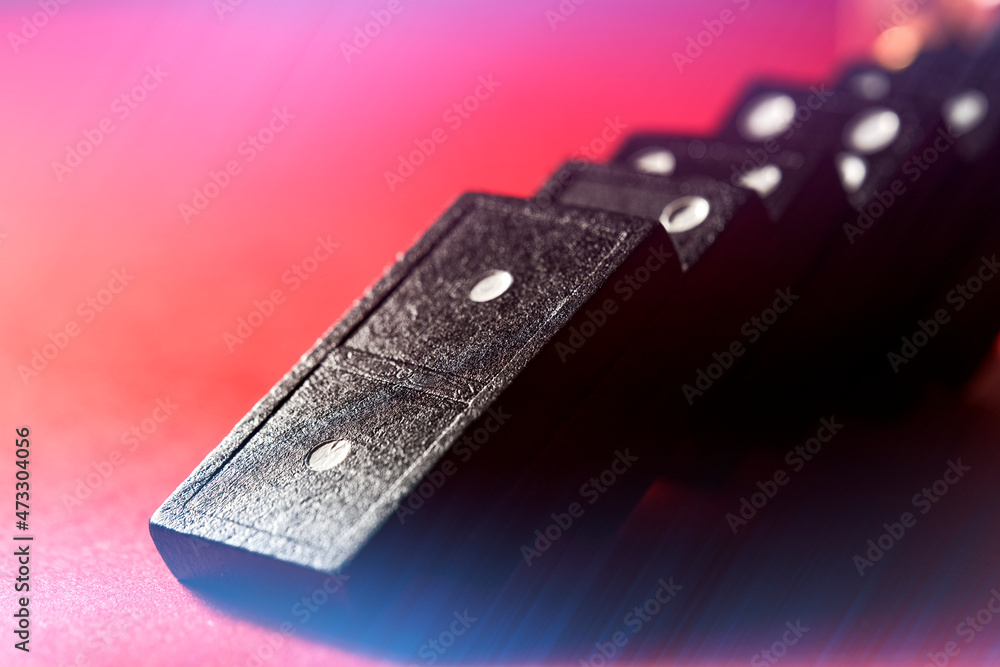 Close up of black dominoes with white dots falling on graded red board, macro Close up of black dominoes with white dots falling on graded red board, macro