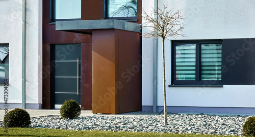 Entrance to a minimalist modern home with a rock garden containing a tree with bare branches